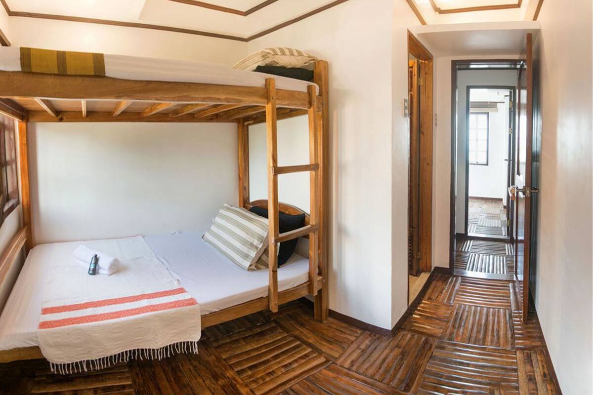 A bunk bed room with a wooden floor, a white wall, and a door leading to another room.