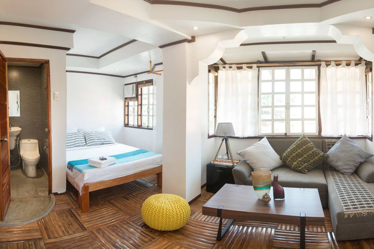 A room with a bed, a sofa, a coffee table, and a window with curtains.