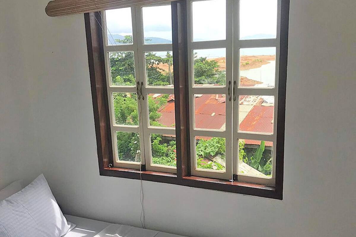 A single-bed room with a large window overlooking a landscape with buildings and greenery.