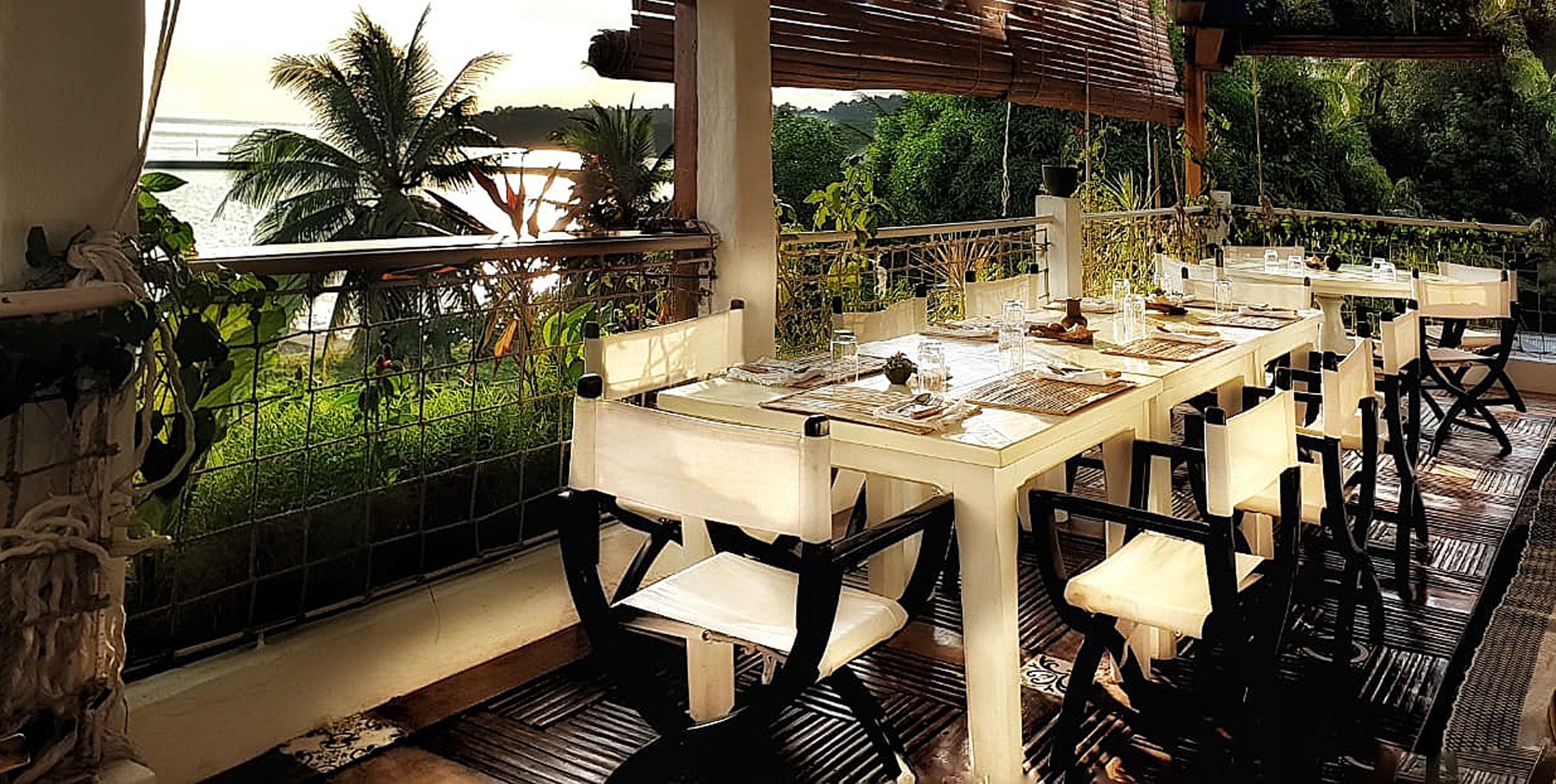 Un espace repas avec des tables et des chaises, une vue sur la mer et une végétation luxuriante.
