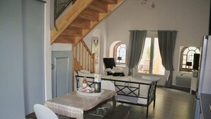Un área de comedor con una mesa dispuesta para dos personas, un banco y una silla. Una escalera conduce a un nivel superior.