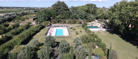 An aerial view of a property with a large rectangular pool surrounded by a well-maintained lawn and various trees.