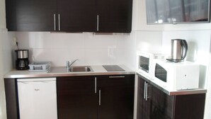 Ett kompakt kök med mörka skåp, en vit bänkskiva, en inbyggd diskmaskin, en kaffebryggare, en vattenkokare och en mikrovågsugn.