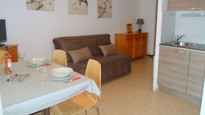 A small, cozy living area with a sofa, a dining table set with plates and glasses, and a kitchenette with a sink and cabinets.
