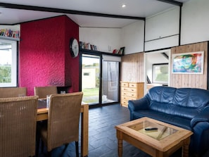 Una sala de estar moderna con una pared texturizada roja, un sofá de cuero azul, una mesa de centro de madera y un comedor con sillas de mimbre y una mesa de madera.