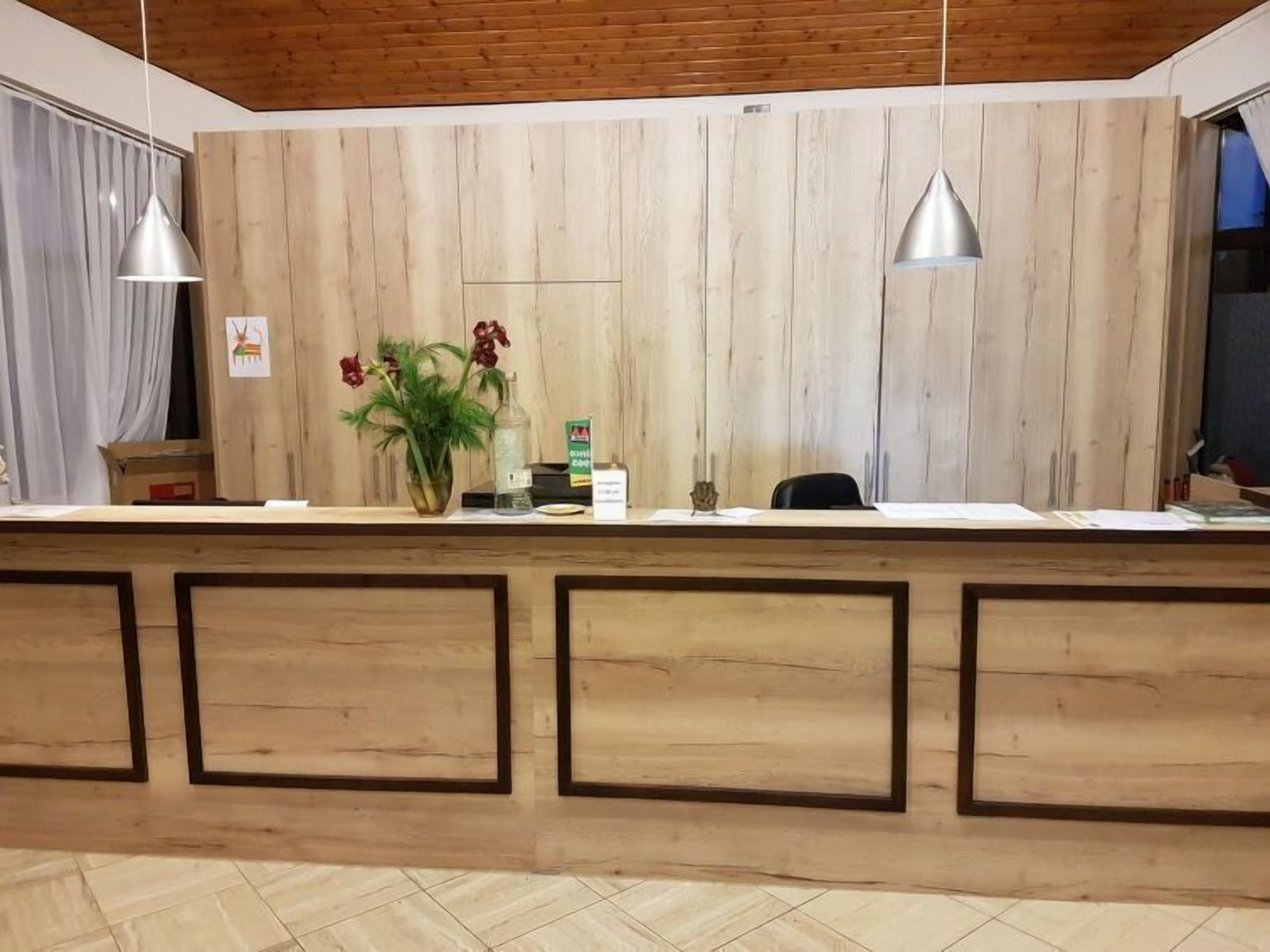A reception desk with a wooden panel backdrop, two pendant lights, a vase with flowers, and a small statue.