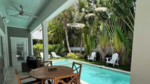 A covered outdoor area with a pool, wooden table, and chairs. - New Luxury-Professionally Decorated Home Pool/Spa 5 Minute walk to AMI ocean (Anna Maria)