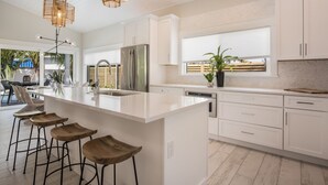 A modern kitchen with a large island, white cabinetry, stainless steel appliances, and a dining area with bar stools. - New Luxury-Professionally Decorated Home Pool/Spa 5 Minute walk to AMI ocean (Anna Maria)