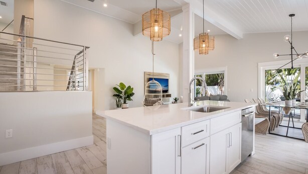 A modern kitchen with white cabinetry, a large island, pendant lights, and a dining area with chairs and a table. - New Luxury-Professionally Decorated Home Pool/Spa 5 Minute walk to AMI ocean (Anna Maria)