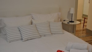 A neatly made bed with white bedding and striped pillows, a small bedside table with a lamp, and a rolled towel and rose on the bed. - Nearby Fortress and close to the center, patio and garden (Firenze)