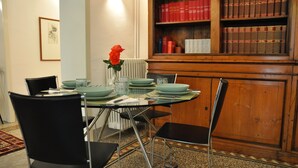A dining area with a table set for four, surrounded by black chairs. A vase with a single red rose is on the table. Behind the table is a wooden bookshelf filled with red and brown books. - Nearby Fortress and close to the center, patio and garden (Firenze)