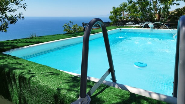 Ein rechteckiger Swimmingpool mit glasklarer, blauer Wasseroberfläche, umgeben von einem gepflegten Rasen und Bäumen.