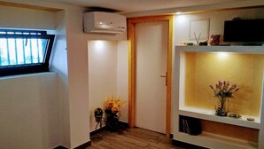Ein kompakter Wohnraum mit Fenster, Klimaanlage, Tür, einem Regal mit Dekoration und einem Fernseher.