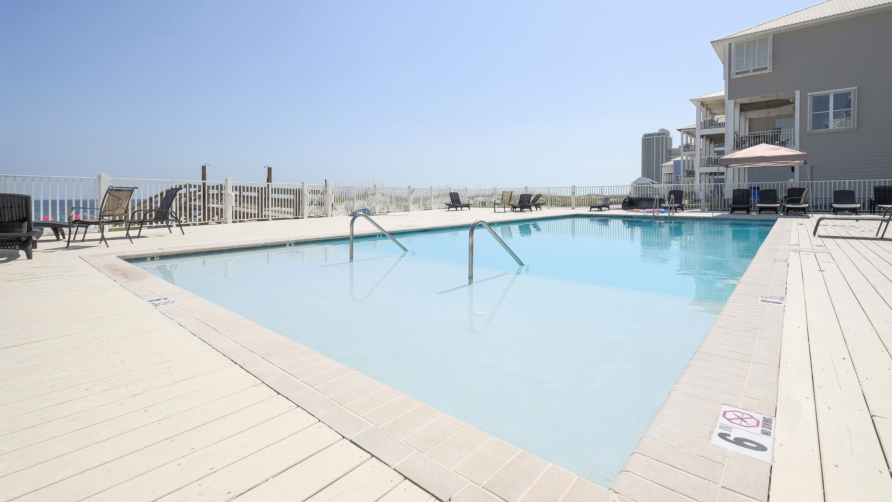 Une piscine avec une terrasse en bois, des chaises longues et une vue sur l’océan.