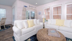 A living room with two white sofas, a starfish-patterned rug, and a woven ottoman. - Beachside Cottage 2BR-3BA. Now booking for Summer! (Orange Beach)