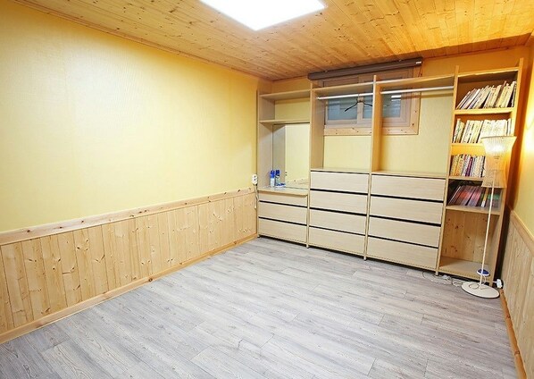 A room with a wooden floor, a wooden ceiling, a yellow wall, a wooden wardrobe, and a bookshelf. - Saryangdo Island Dandihae Pension (Tongyeong)