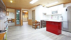 Une cuisine moderne avec un îlot central rouge, un plancher en bois et un ventilateur près de l’entrée.