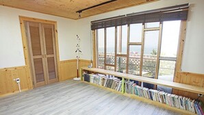 Une pièce dotée d’un plancher en bois, d’une grande fenêtre offrant une belle vue, d’une bibliothèque et d’une porte avec des volets.