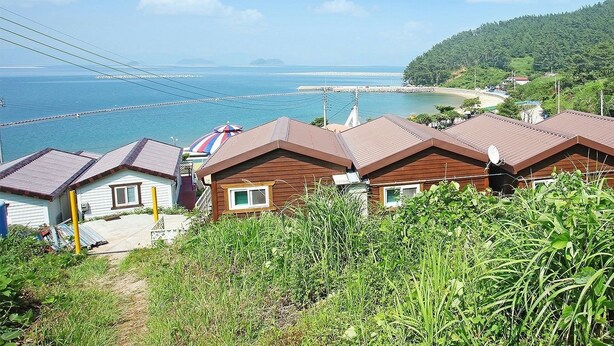 Une zone côtière avec des maisons donnant sur la mer, un pont et une colline boisée.