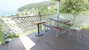 Une terrasse extérieure avec une table et des bancs en bois, une vue dégagée sur la mer et les collines, et une clôture blanche en treillis.
