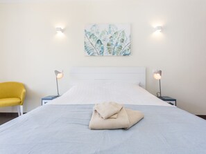 Un letto ben rifatto con una coperta piegata, una sedia gialla e due abat-jour.