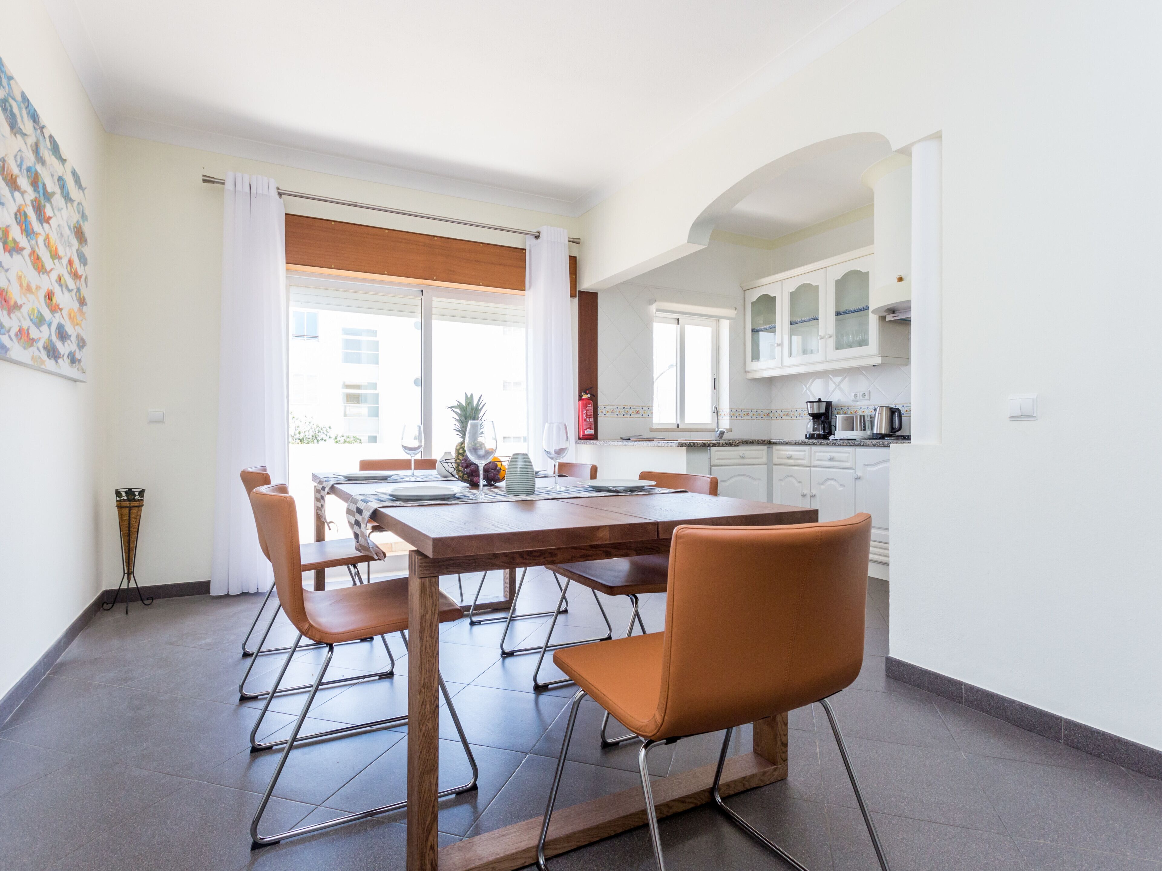 Una cocina moderna con armarios blancos, una mesa de comedor para cuatro personas y vistas a la ciudad a través de amplios ventanales.