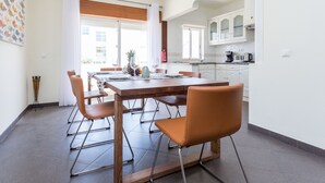 A modern kitchen with white cabinets, a dining table set for four, and a view of the city through large windows.