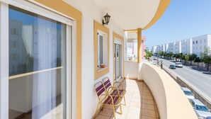 A balcony with a view of a street and buildings. There are two chairs and a small table.
