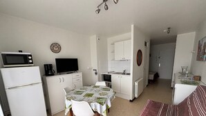 A compact living space with a kitchenette, a dining area with a table and chairs, a sofa, and a television. - Cozy apartment facing Thau pond, pet friendly (Balaruc-les-Bains)