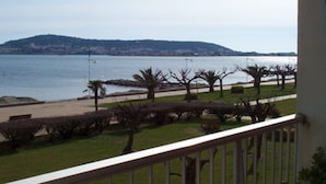 A balcony with a view of a beach, a grassy area with trees, and a distant hill. - Cozy apartment facing Thau pond, pet friendly (Balaruc-les-Bains)