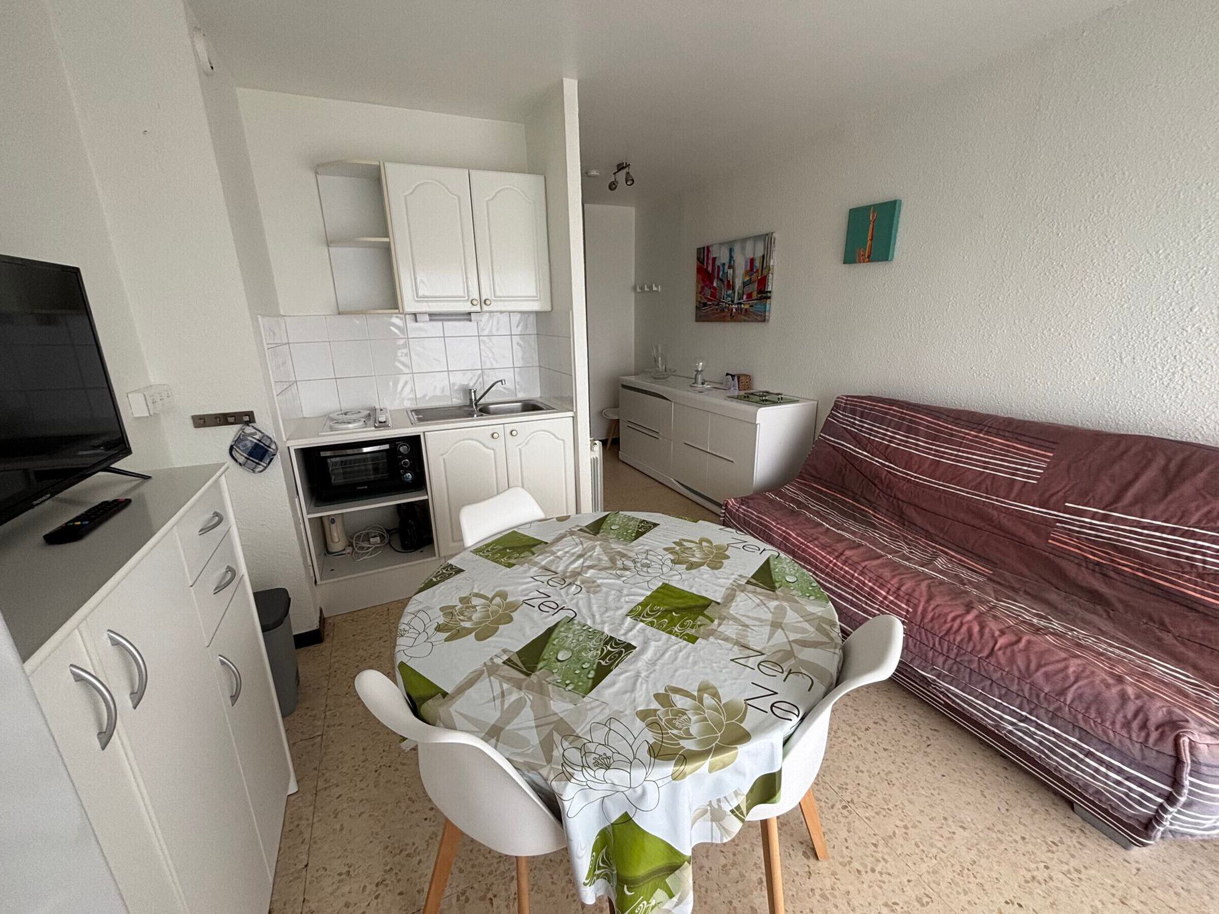 Quarto compacto com cozinha compacta, área de refeições com mesa e cadeiras, cama e televisão.