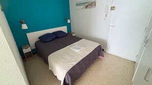 A bedroom with a bed, a nightstand, a lamp, a door, and a wall with a picture. - Cozy apartment facing Thau pond, pet friendly (Balaruc-les-Bains)