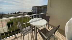 A balcony with a table and chairs, overlooking a body of water and a distant city skyline.