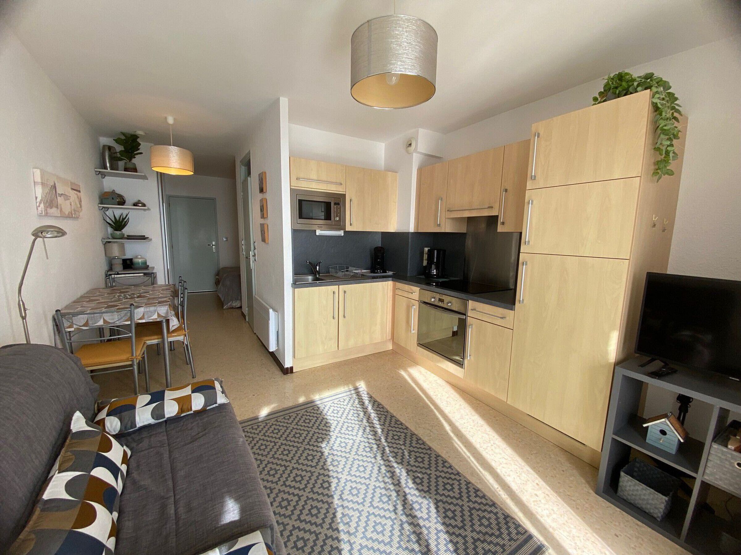 Un espacio habitable compacto con kitchenette, zona de comedor y sala de estar con sofá y mueble para televisión.