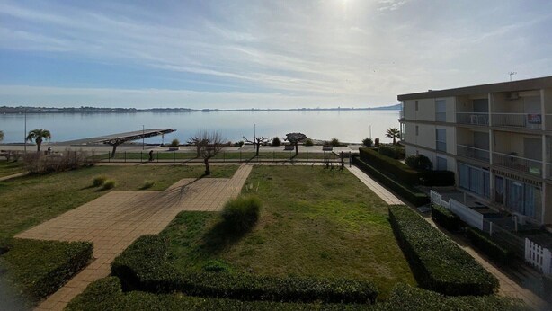 A view of a waterfront property with a paved walkway, a grassy area, and a building with balconies.