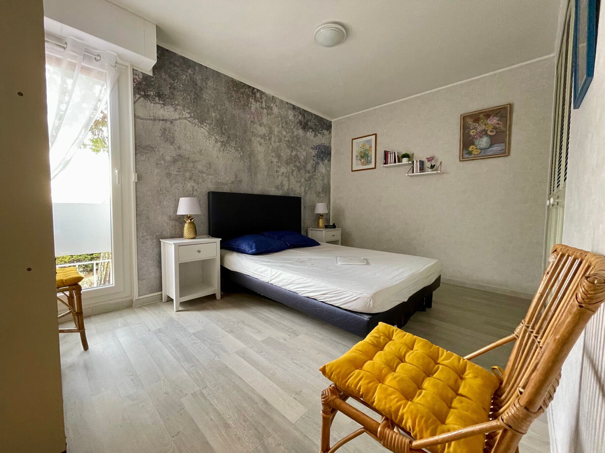 A bedroom with a bed, nightstands, a chair, and a view of the outdoors.