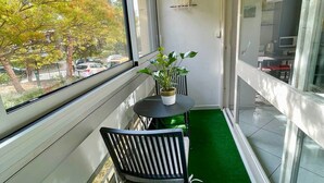 Un balcón con césped artificial verde, una planta en maceta y una silla.