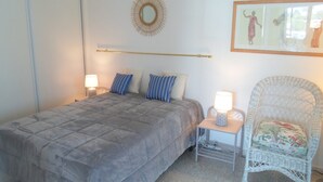 A bedroom with a bed, two bedside lamps, a wicker chair, and a wall-mounted mirror.