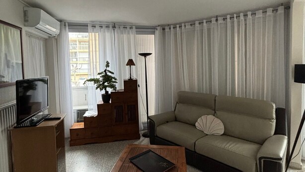 A living room with a sofa, a small table, a TV, a plant, and a lamp.