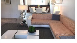 Un salon moderne avec un canapé d’angle, une table basse en verre et un coin repas comprenant une table et des chaises.