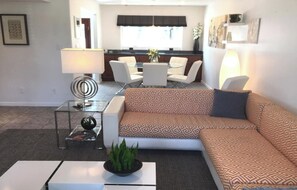 Un salon moderne avec un canapé d’angle, une table basse en verre et un coin repas avec des chaises.