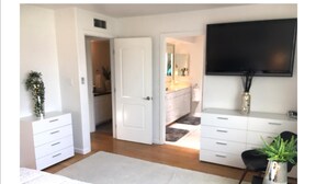 Une chambre à coucher avec un lit, une commode, une télévision et une plante.