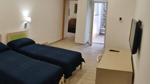 Ein Hotelzimmer mit zwei Einzelbetten, einem Schreibtisch, einem Sessel und einem an der Wand befestigten Fernseher.