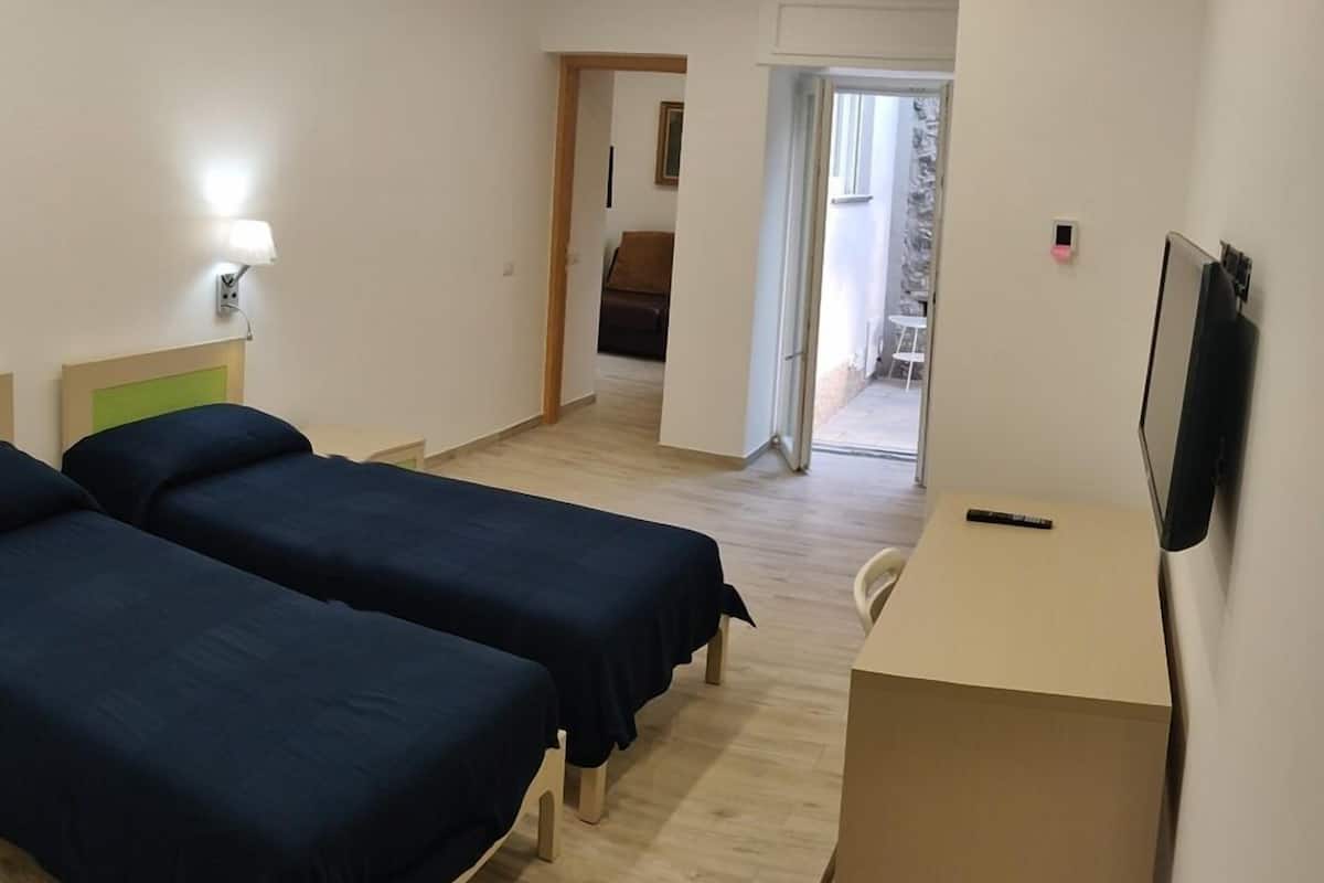 A hotel room with two single beds, a desk, a chair, and a TV mounted on the wall.