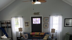 Ein geräumiges Wohnzimmer mit hoher Decke, einem Deckenventilator, einem blauen Sofa, einem weißen Couchtisch und einem Korbwannenkorb.