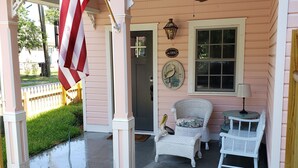 Ein rosafarbenes Haus mit Veranda, einer amerikanischen Flagge, einem Willkommensschild und Korbmöbeln.