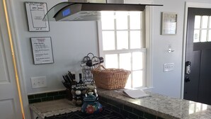 Eine Küche mit Gasherd, Backofen und einer Edelstahl-Dunstabzugshaube. Ein Fenster mit Jalousien, ein Korb auf der Arbeitsplatte und ein wandmontierter Messerblock sind vorhanden.