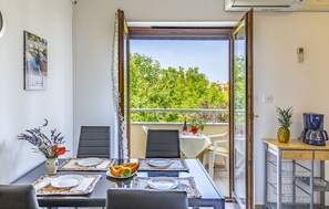 A dining area with a table set for two, a vase with flowers, and a view of greenery outside. - Apartments Lorencin Milka (Medulin)
