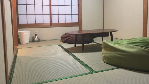 A traditional Japanese room with tatami flooring, a low table, a green futon, and a shoji screen window. - Hanazono Kita Terrace House (Osaka)