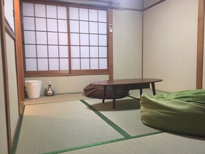 A traditional Japanese room with tatami flooring, a low table, a green futon, and a shoji screen window. - Hanazono Kita Terrace House (Osaka)